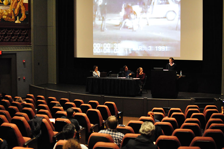 Three panelists and a moderator are on stage at the IU Cinema. They're showing a film clip.