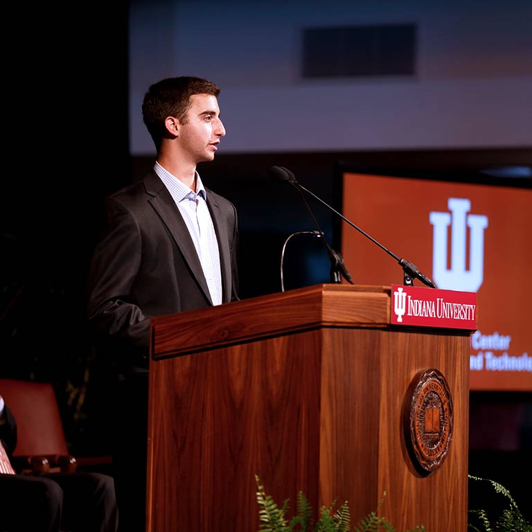 A student in a suit gives a speech at a podium.