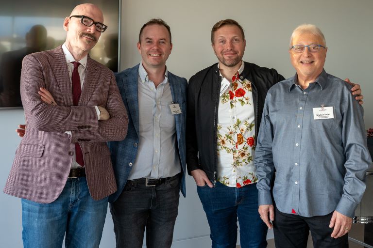 Four people stand next to one another smiling at the camera.